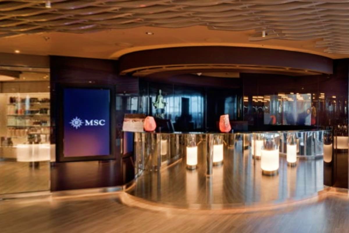 Modern MSC cruise ship reception desk with illuminated counter, digital display showing MSC logo, and contemporary interior d