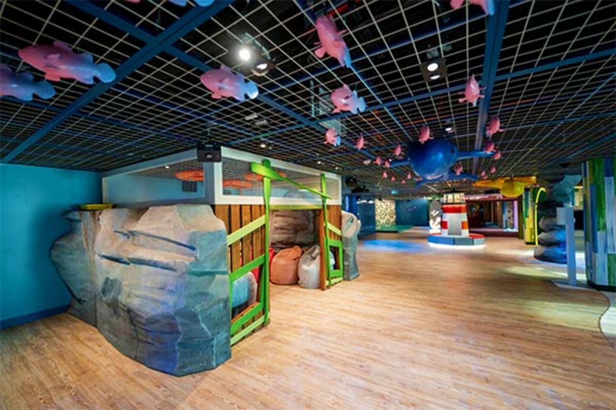 Colorful indoor play area with rock climbing wall, suspended fish decorations, and interactive exhibits aboard cruise ship