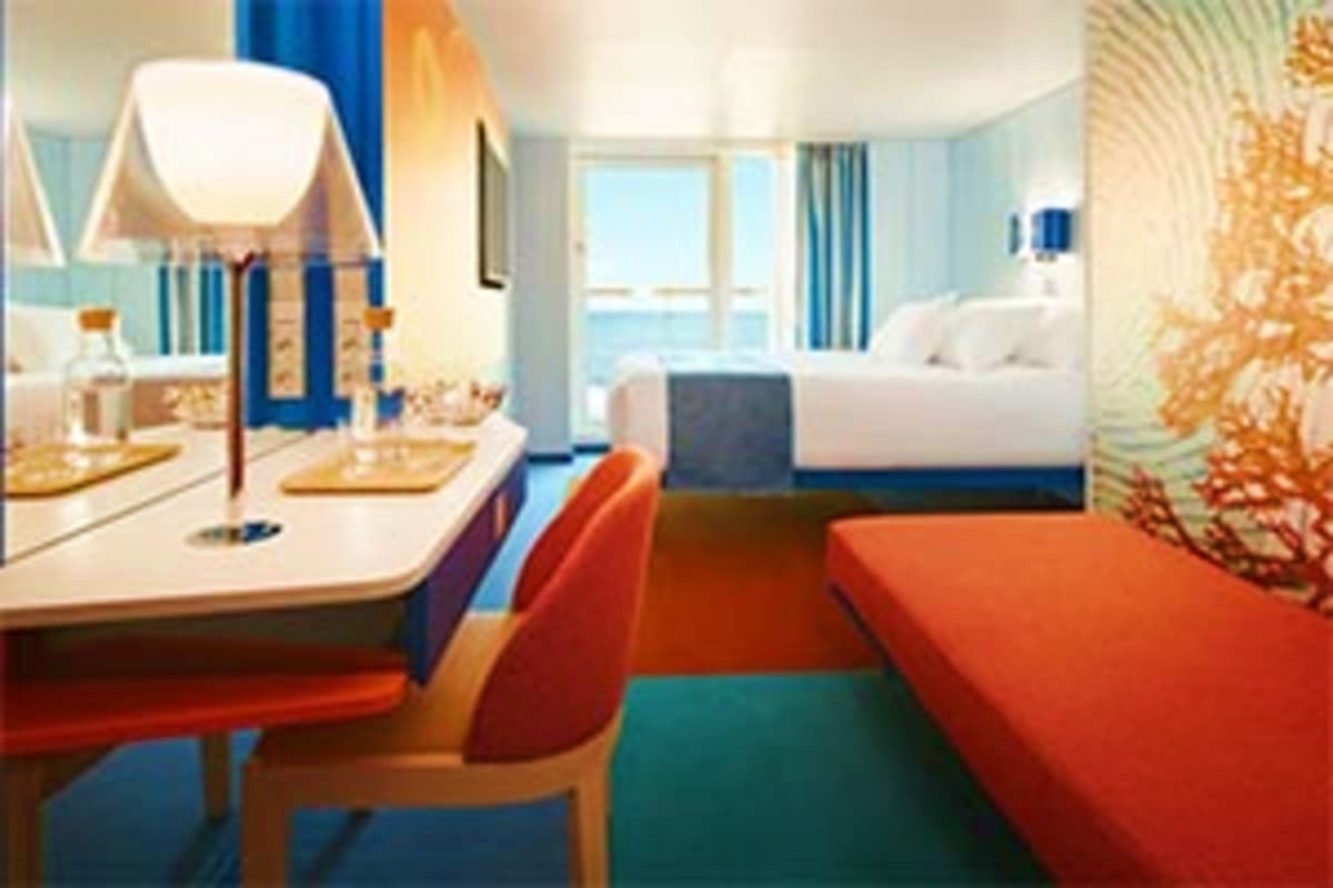 Modern cruise ship cabin with dual beds, desk area, ocean view windows, and contemporary blue and orange décor