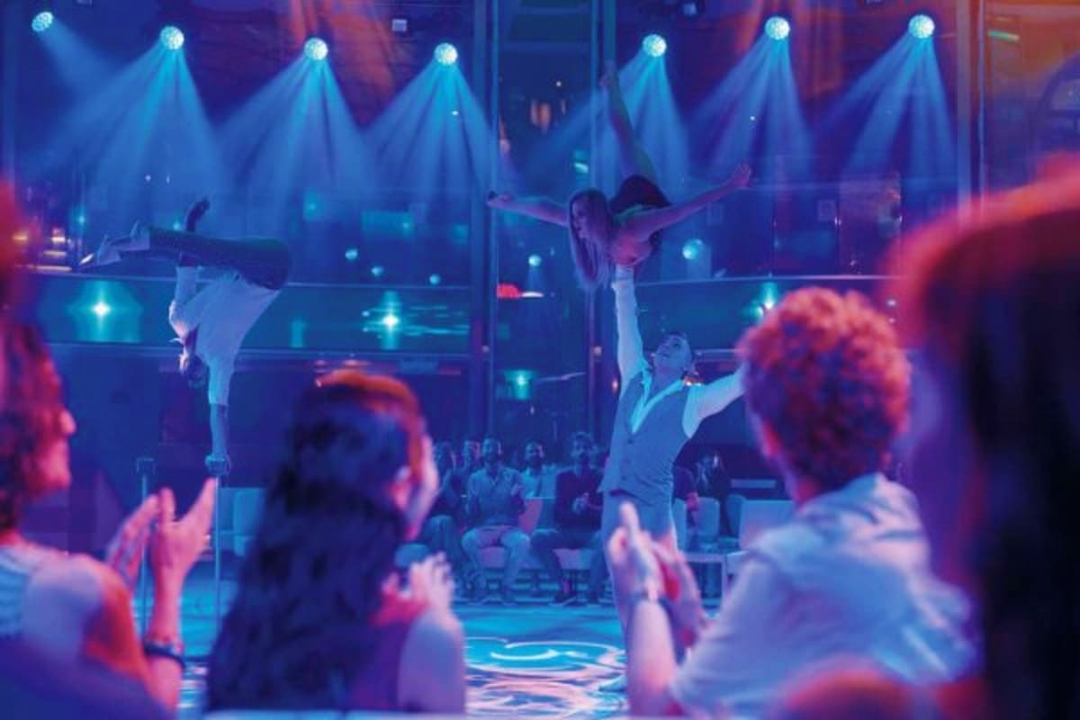 Acrobatic performers on stage under blue spotlights during evening entertainment on a cruise ship with audience watching.