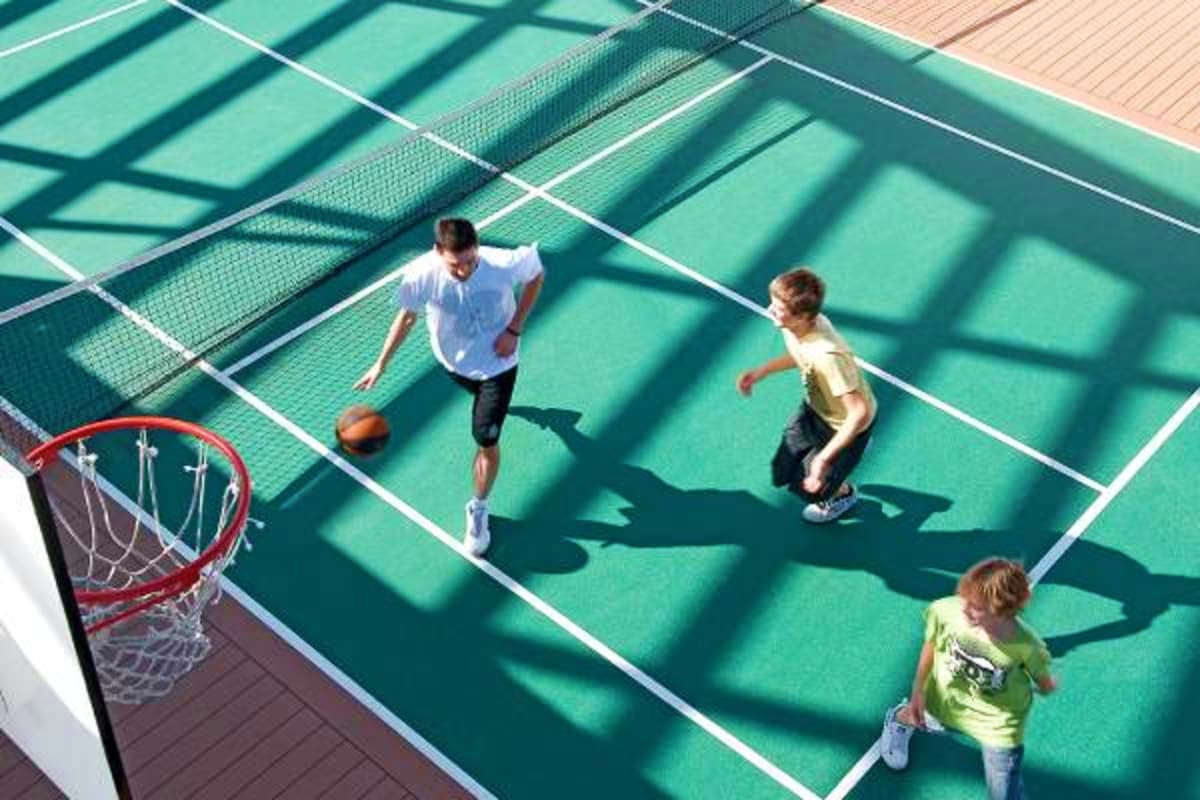 Overhead view of three people playing basketball on outdoor courts on a cruise ship deck with red hoop visible