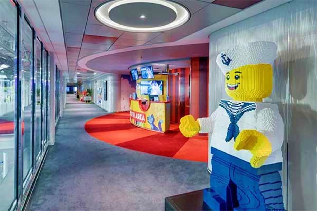 Modern cruise ship corridor with colorful LEGO character decoration, red carpet, illuminated ceiling, and entertainment venue