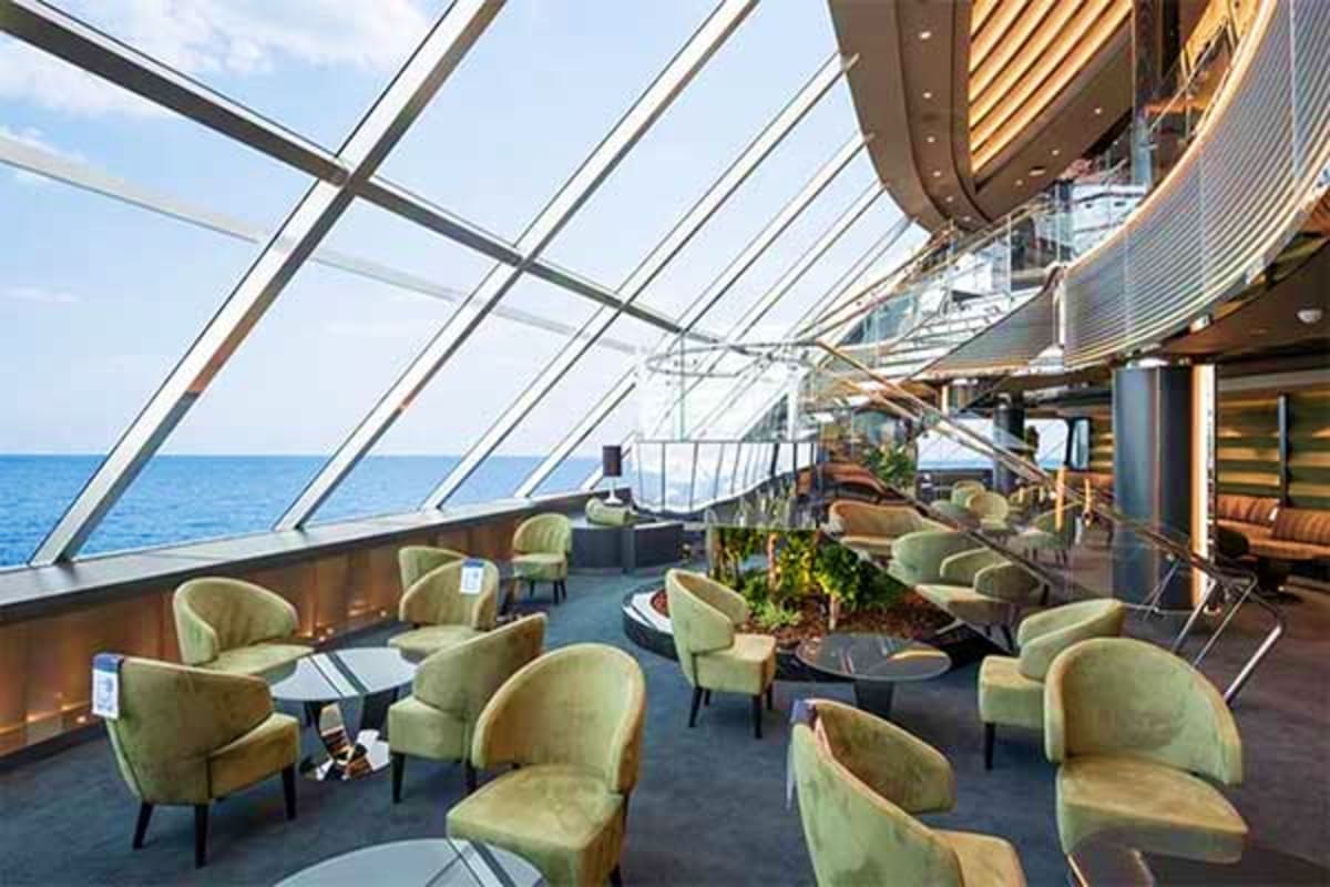 Modern cruise ship lounge with floor-to-ceiling windows overlooking ocean, beige armchairs, and sea view