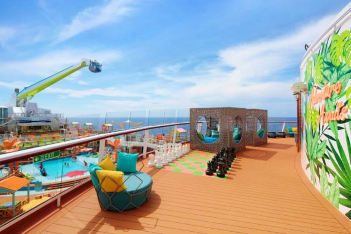 Cruise ship deck with pool, colorful playground equipment, and ocean view overlooking coastal city