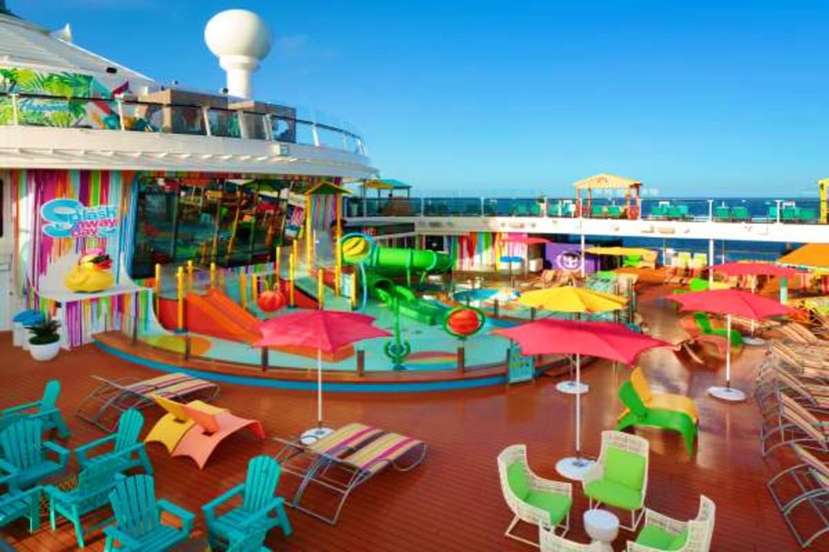 Colorful waterpark deck on cruise ship with slides, pools, umbrellas, and lounge chairs overlooking ocean