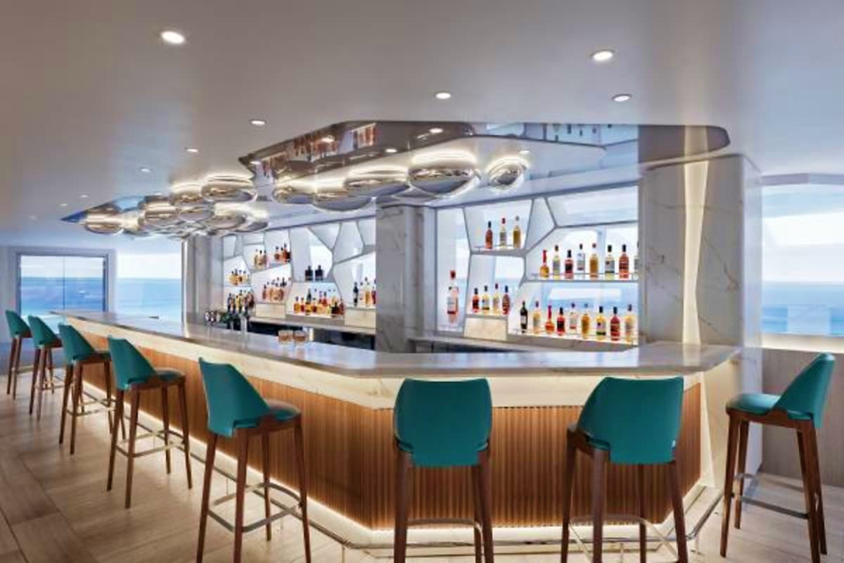 Modern cruise ship bar with teal seating, illuminated liquor shelves, and ocean views through floor-to-ceiling windows