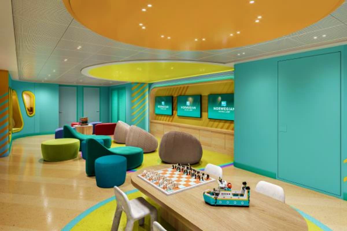 Modern kids' playroom on Norwegian Cruise ship with turquoise walls, colorful bean bag chairs, chess board, toy ship, and ent