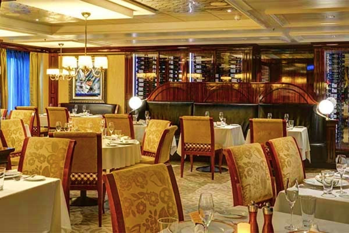 Elegant fine dining restaurant interior with gold and red upholstered chairs, white tablecloths, and wood-paneled wine cellar