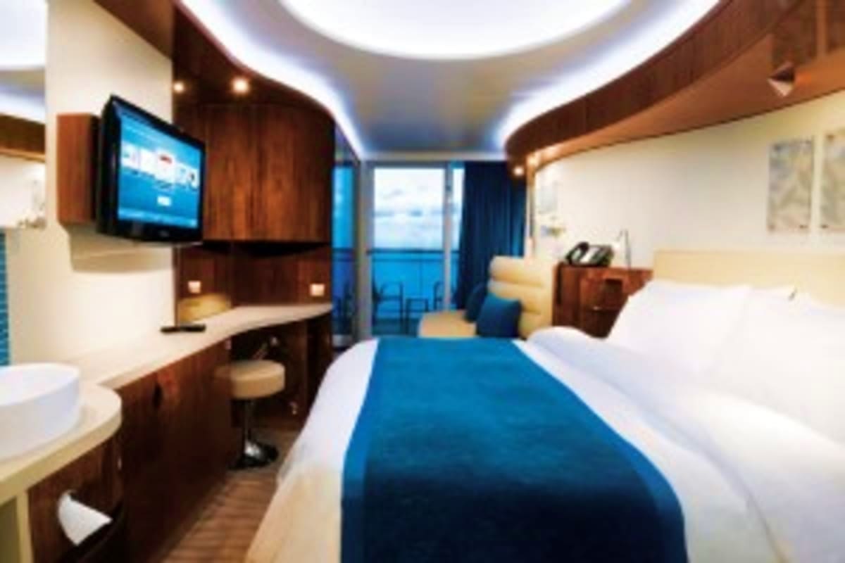 Norwegian Epic Southern Europe Cruise Modern cruise ship cabin with blue bedding, flat-screen TV, dark wood furnishings, and ocean view balcony