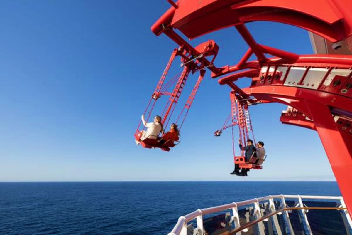 Passengers enjoying red swingboat rides on MSC World America cruise ship deck over ocean water