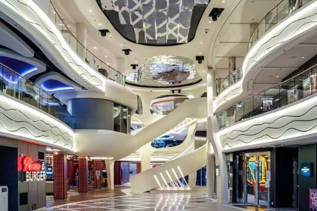 Modern multi-level shopping mall interior with curved white architecture, LED lighting, escalators, and retail storefronts on