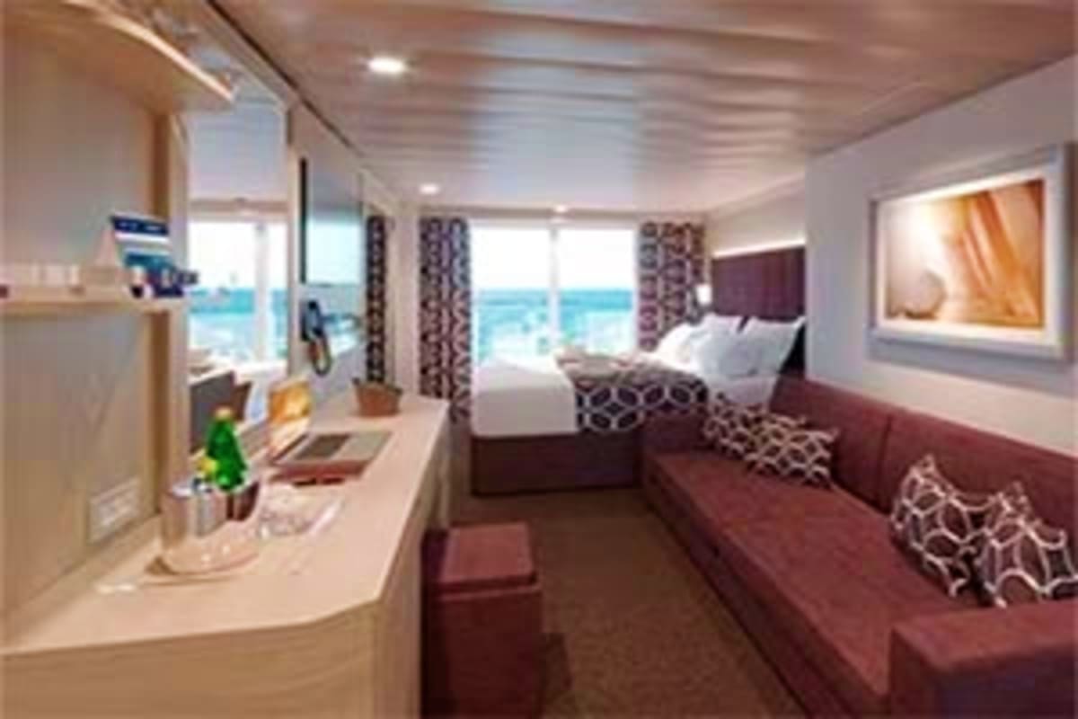 Luxury cruise ship stateroom with ocean view, queen bed, sitting area, and modern furnishings overlooking the sea