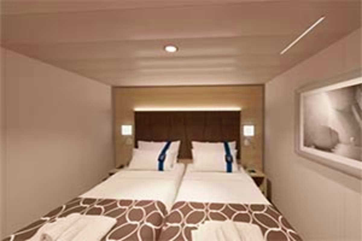 Modern cruise ship cabin with twin beds, dark wood headboard, beige walls, recessed lighting, and porthole window showing oce