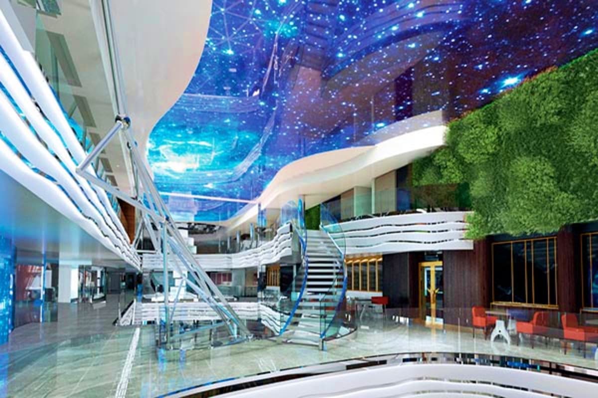 MSC World Europa Barcelona Roundtrip Cruise Modern cruise ship interior atrium with illuminated blue starry ceiling, white curved architecture, stairs, and green living