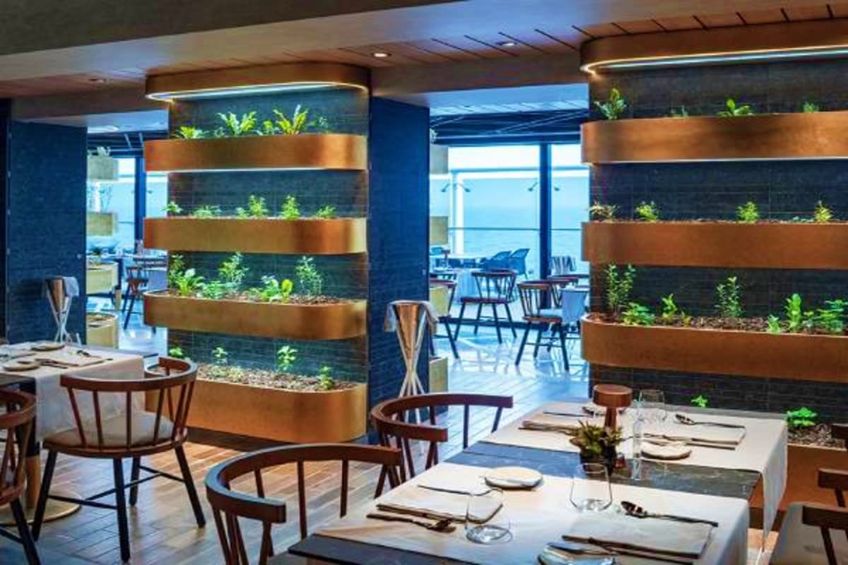 Modern upscale restaurant interior with tiered copper planter boxes, ocean view windows, and elegantly set dining tables with
