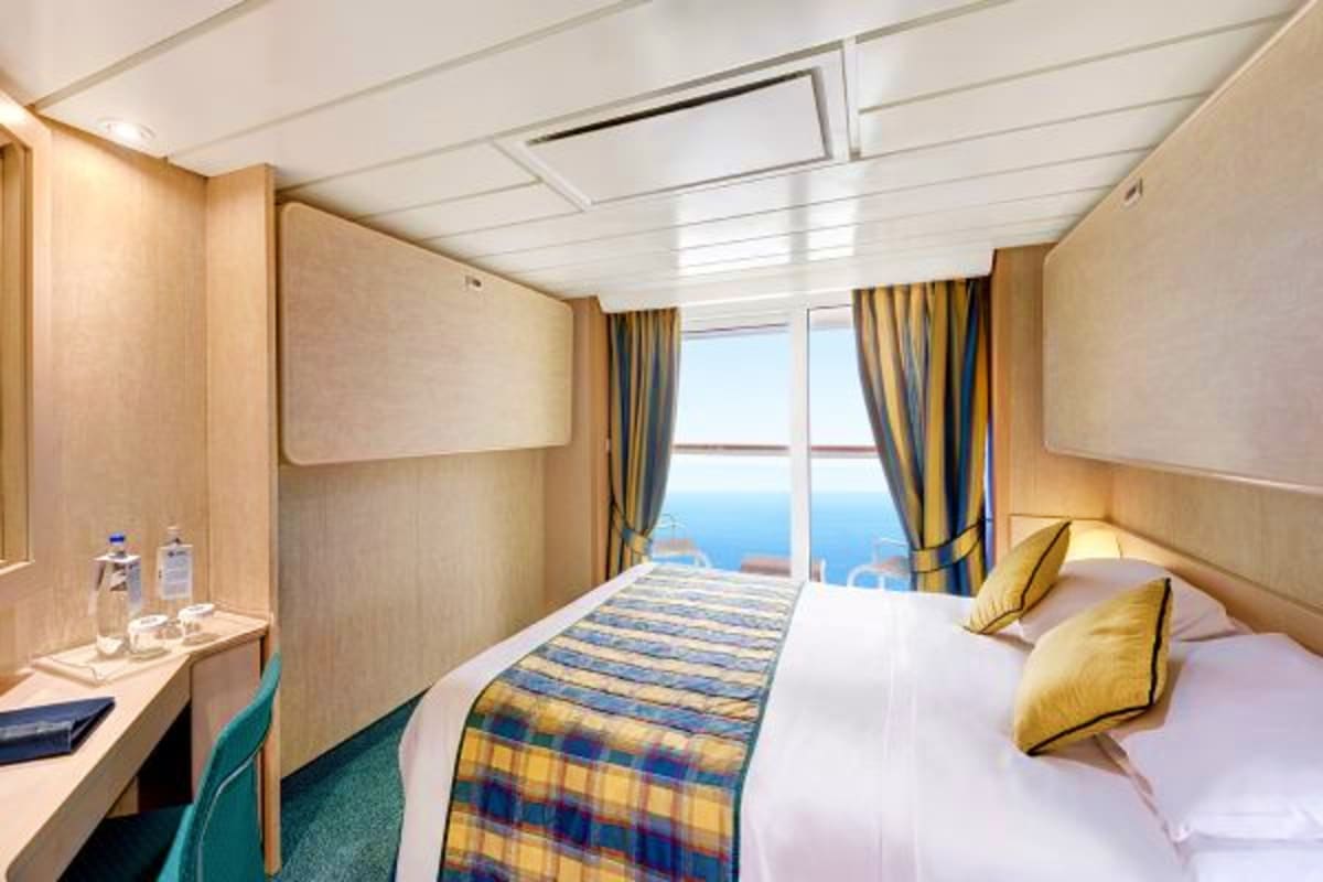 MSC Fantasia Eastern Mediterranean Cruise Luxury cruise ship interior stateroom with ocean view, queen bed with gold pillows, desk, and large window overlooking blue s