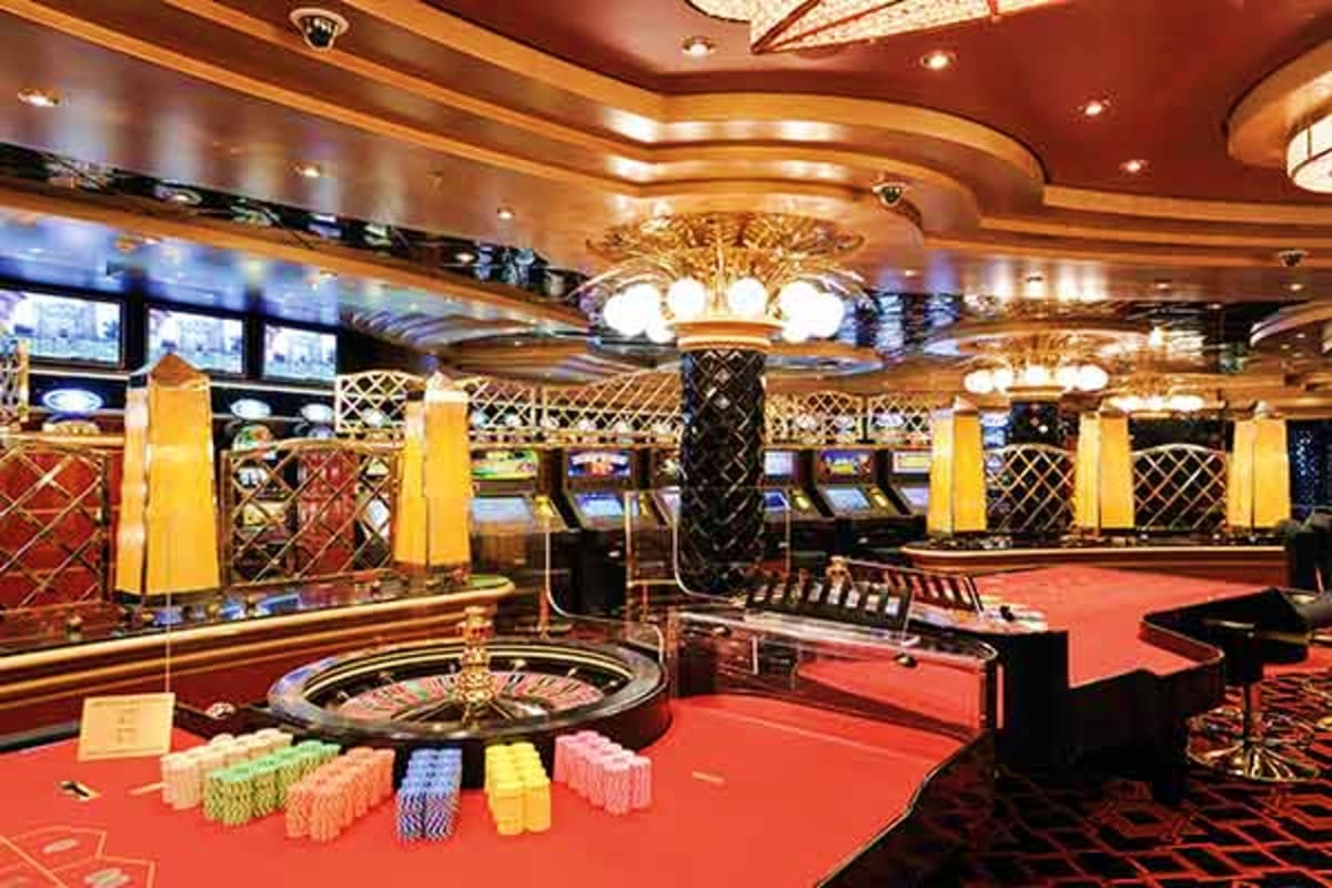 MSC Fantasia Eastern Mediterranean Cruise Luxury casino interior with roulette table, poker chips, slot machines, and ornate gold ceiling fixtures on red carpeting