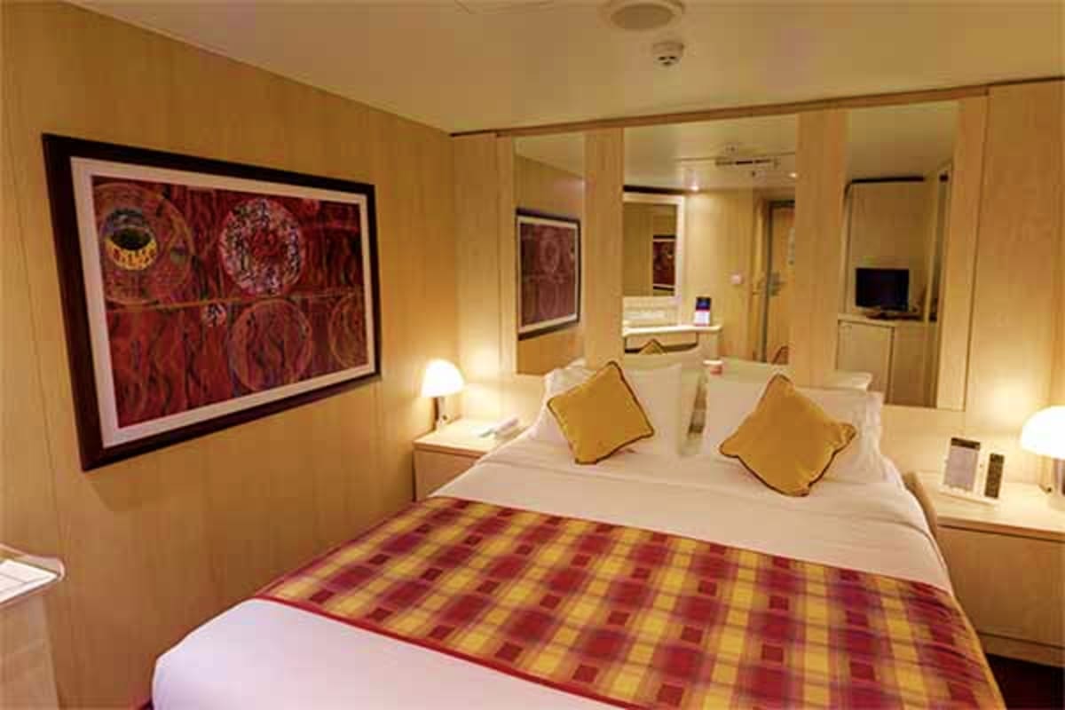 MSC Fantasia Eastern Mediterranean Cruise Modern cruise ship cabin with queen bed, gold pillows, red plaid bedding, warm lighting, framed red artwork, and en-suite bat