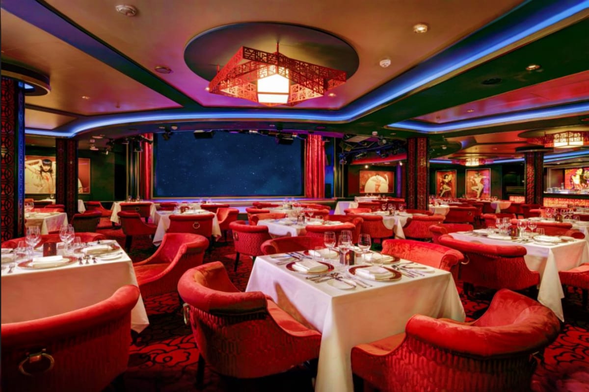 Elegant cruise ship dining room with red velvet chairs, white tablecloths, and ocean view windows at night
