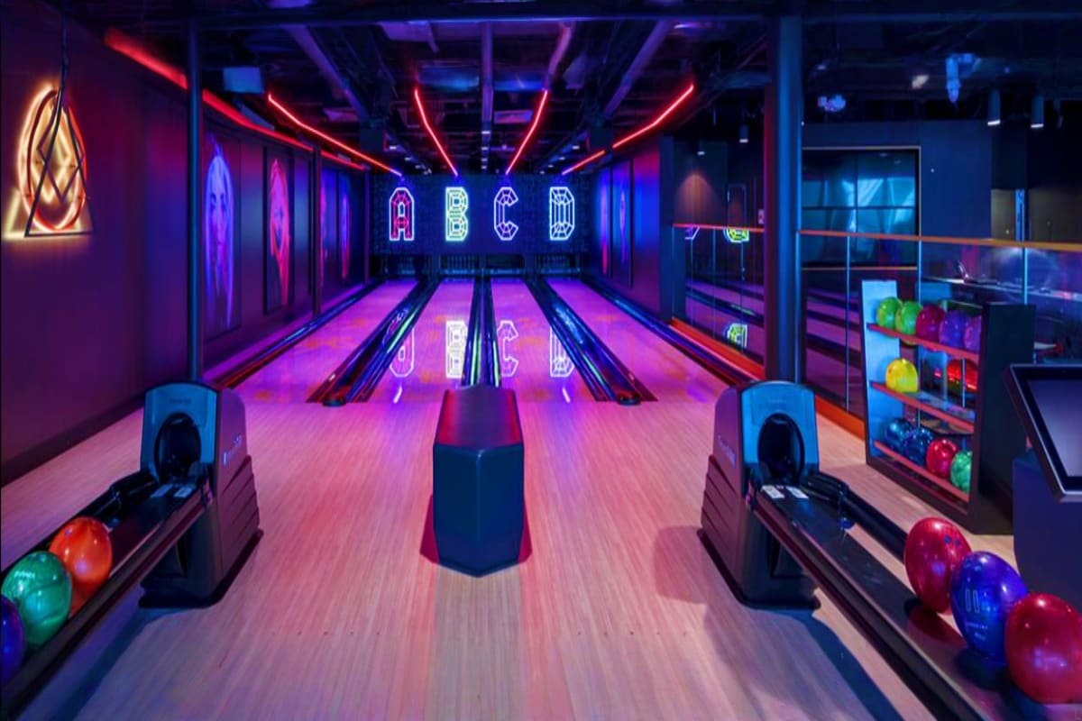 Modern bowling alley with neon purple and pink lighting, multiple lanes with colorful bowling balls, and ABCD neon sign on wa