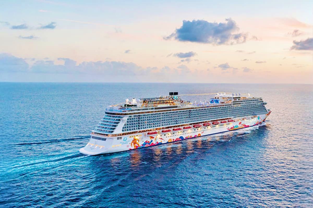 Large modern cruise ship sailing on blue ocean water with colorful hull design against cloudy sky at sunset
