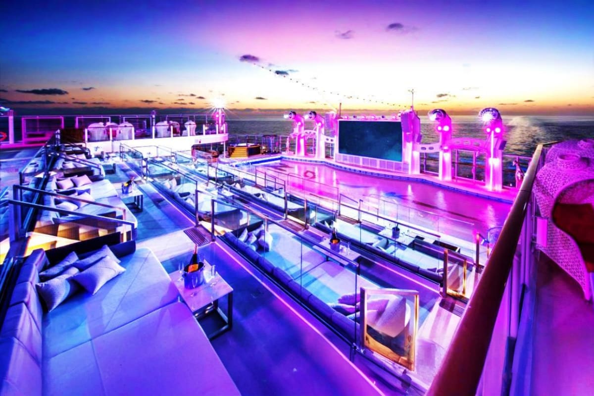 Genting Dream cruise ship deck at sunset with neon pink lighting, lounge seating, and ocean view at dusk