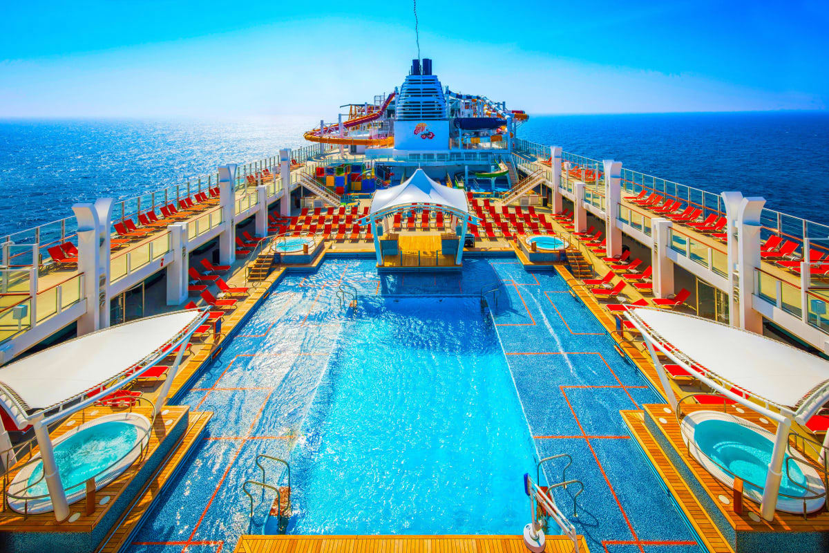 Aerial view of cruise ship deck with swimming pool, red lounge chairs, and ocean horizon on Genting Dream vessel