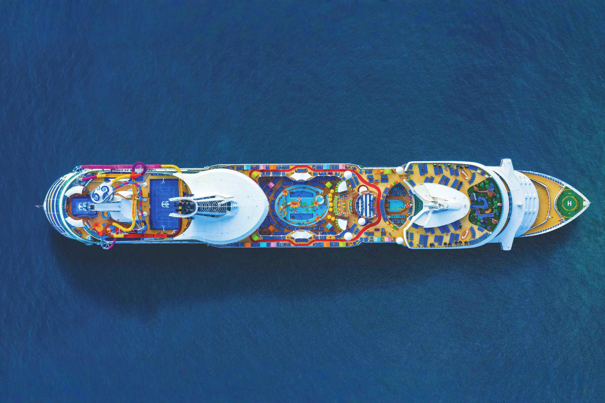 Aerial view of Navigator of the Seas cruise ship in blue ocean water showing colorful deck layout and pools from above
