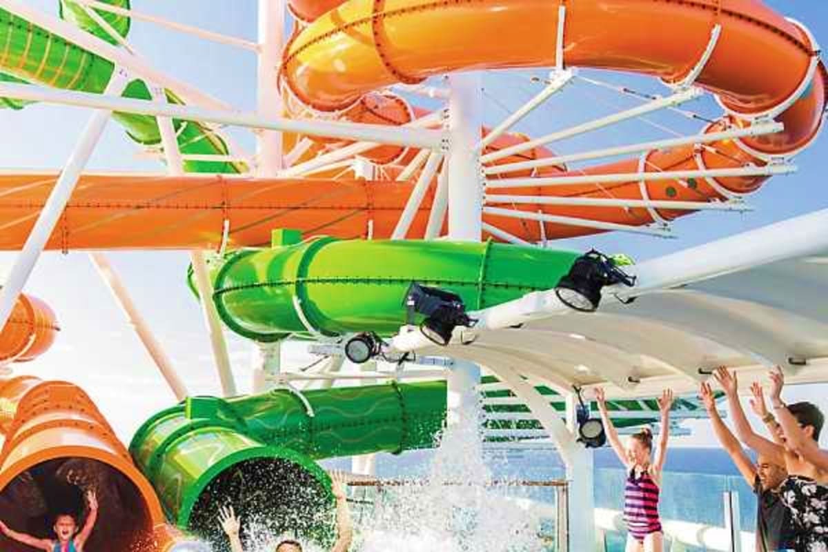 Water slide complex with orange and green tube slides on cruise ship, passengers enjoying waterpark activities with ocean vie