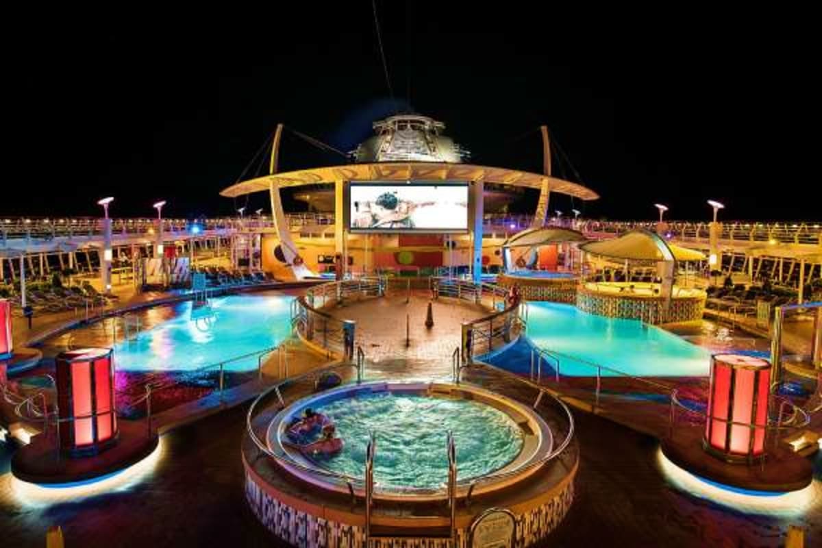 Illuminated nighttime view of Liberty of the Seas cruise ship pool deck with multiple pools, hot tubs, and entertainment venu