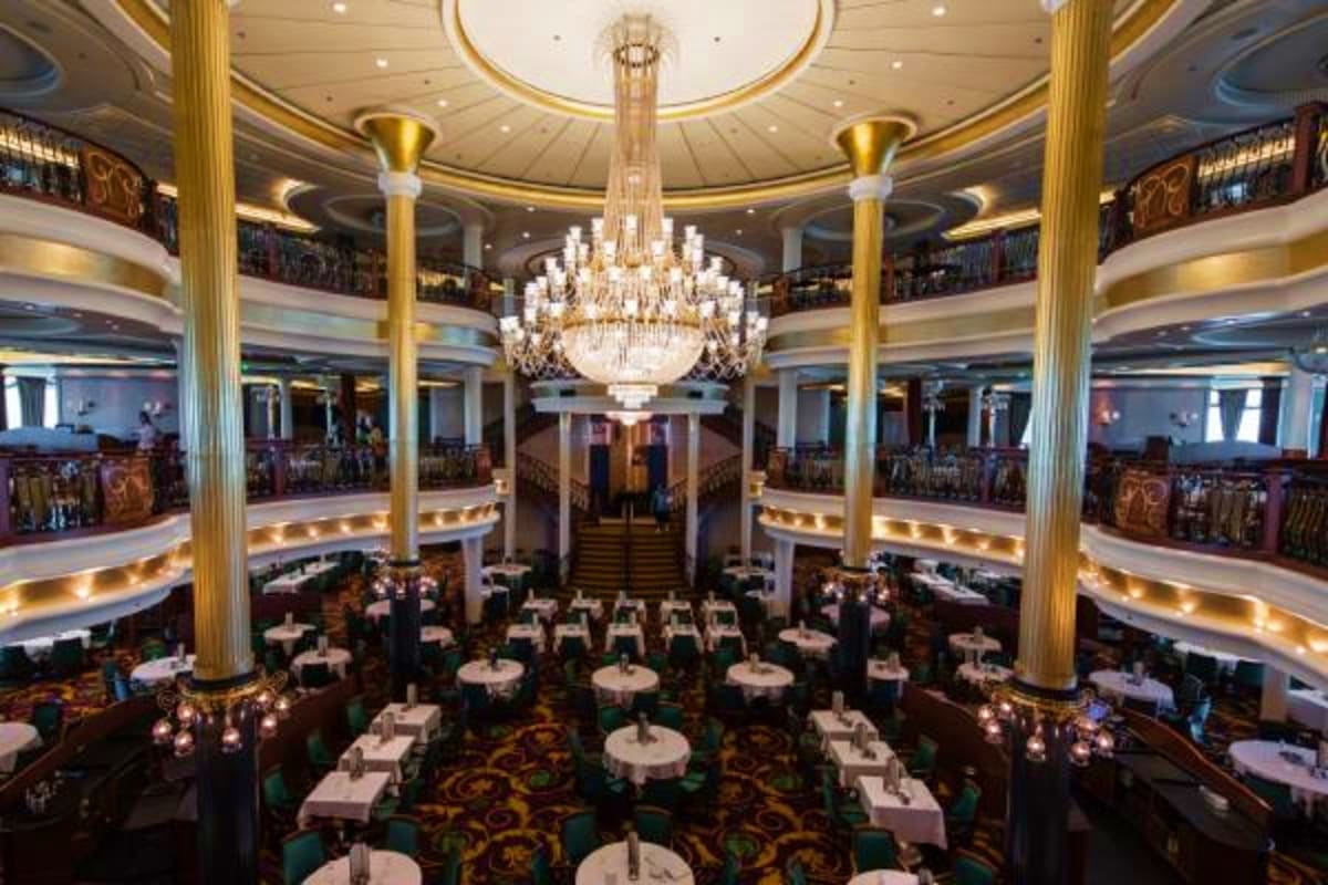 Elegant multi-level dining room with ornate chandelier, gold columns, and formal table settings on cruise ship Liberty of the