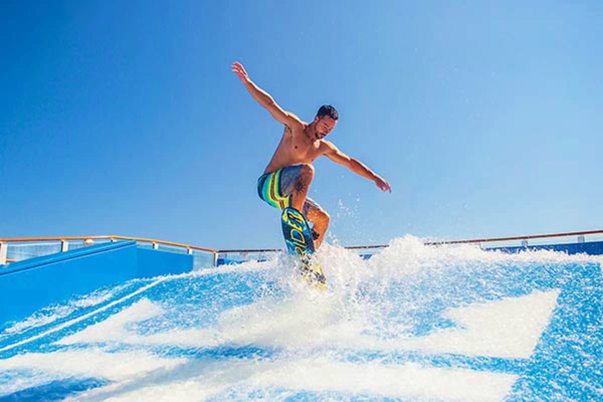 Shirtless man surfing on artificial wave pool with arms outstretched on cruise ship