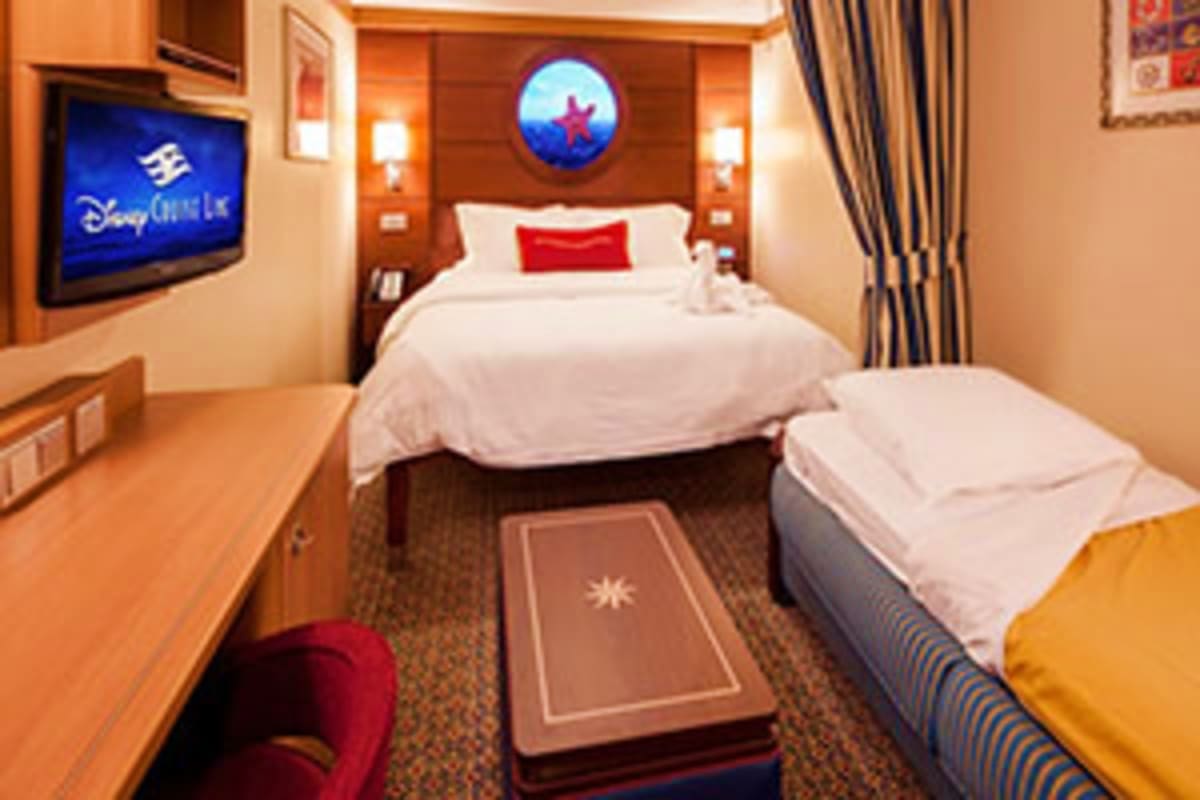 Disney Dream cruise ship cabin with two beds, wall-mounted TV, porthole window with red star design, and warm orange wood acc