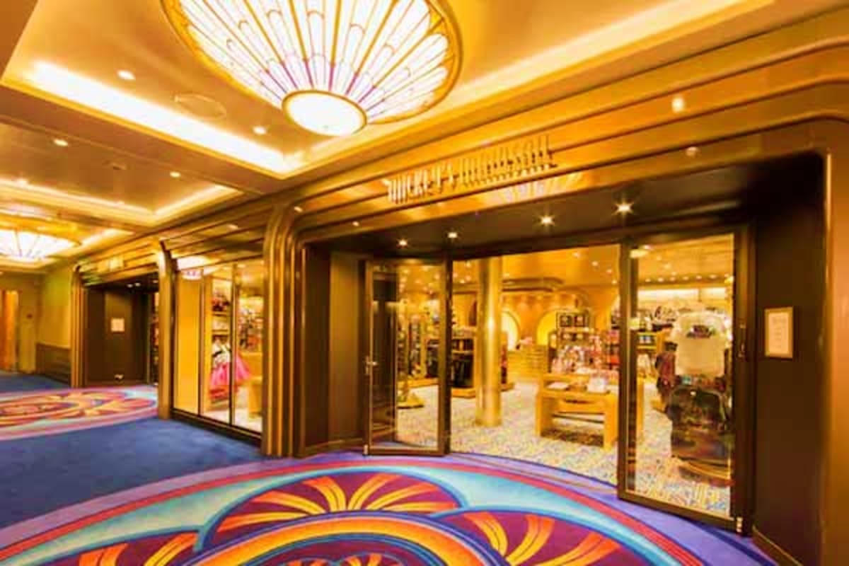 Elegant cruise ship corridor with gold-trimmed ceiling, decorative lighting fixture, and colorful floor design leading to ret