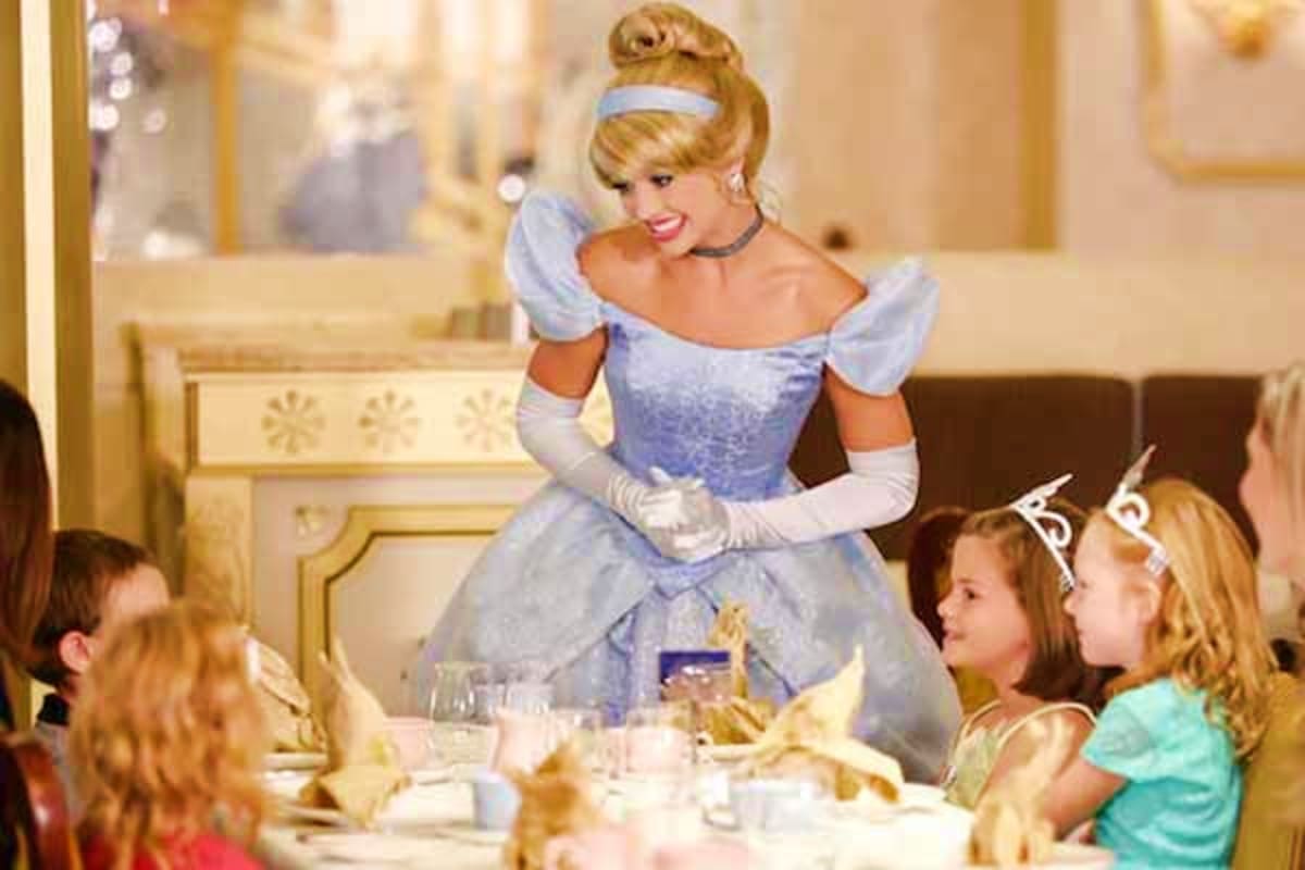 Cinderella character in blue ball gown greeting children at formal dining table during Disney cruise ship event