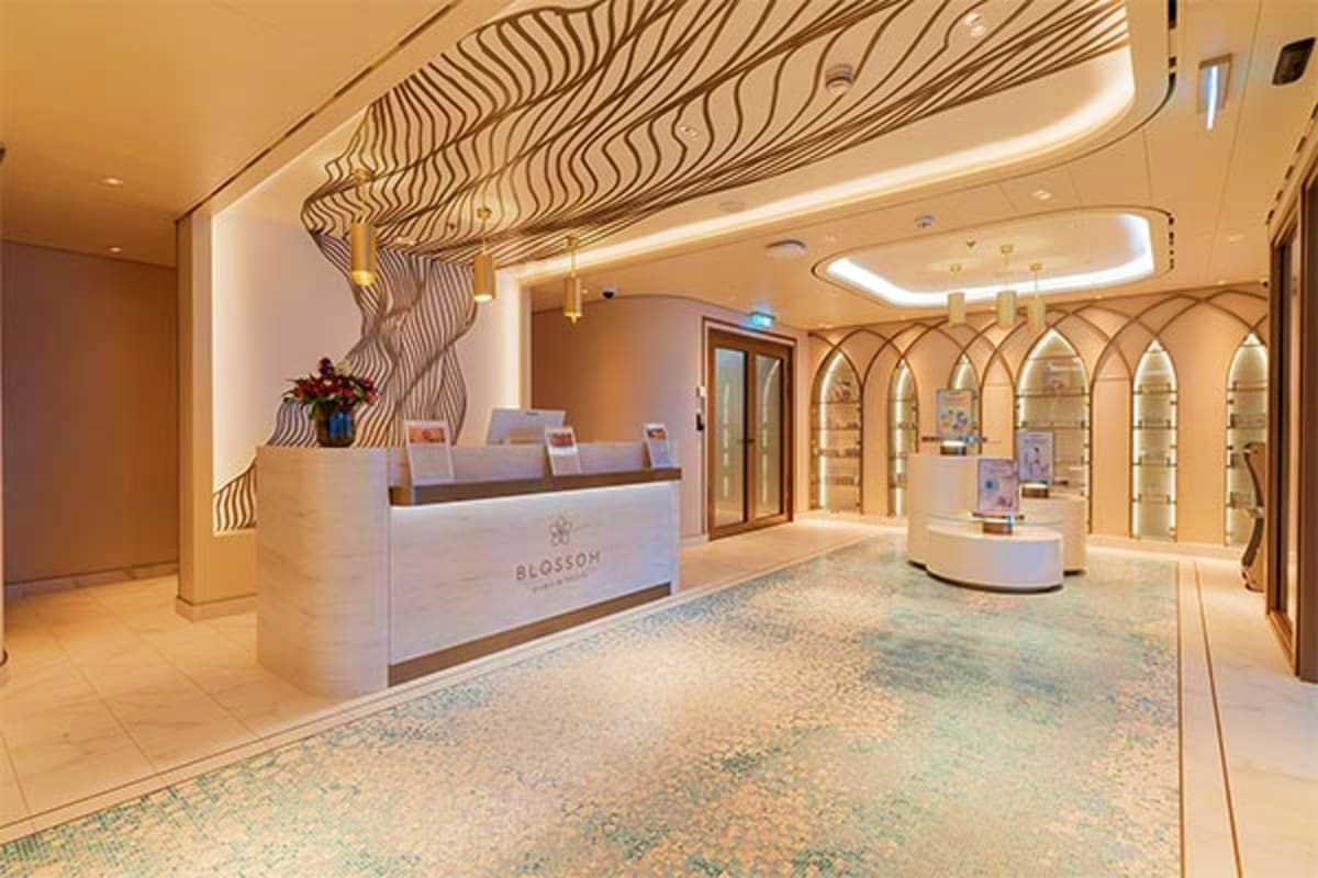 Aroya Mediterranean Cruise Luxury spa reception area with white marble desk, geometric wood ceiling feature, and illuminated product display cases