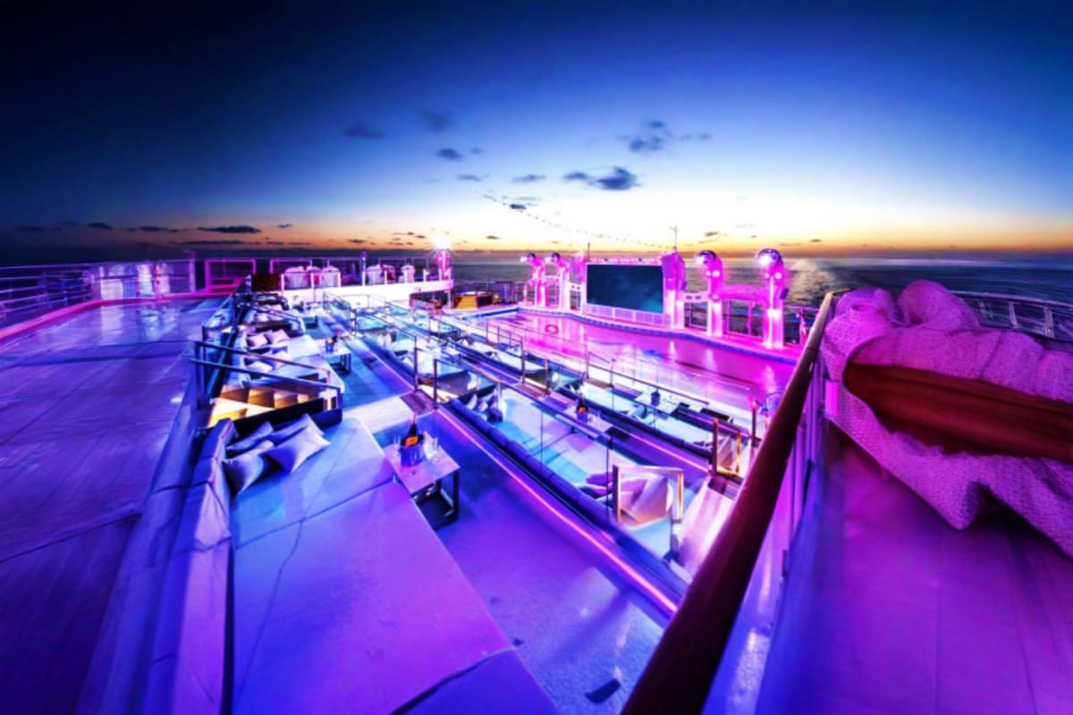 Cruise ship deck at sunset with purple neon lighting, lounge chairs, and ocean horizon at dusk