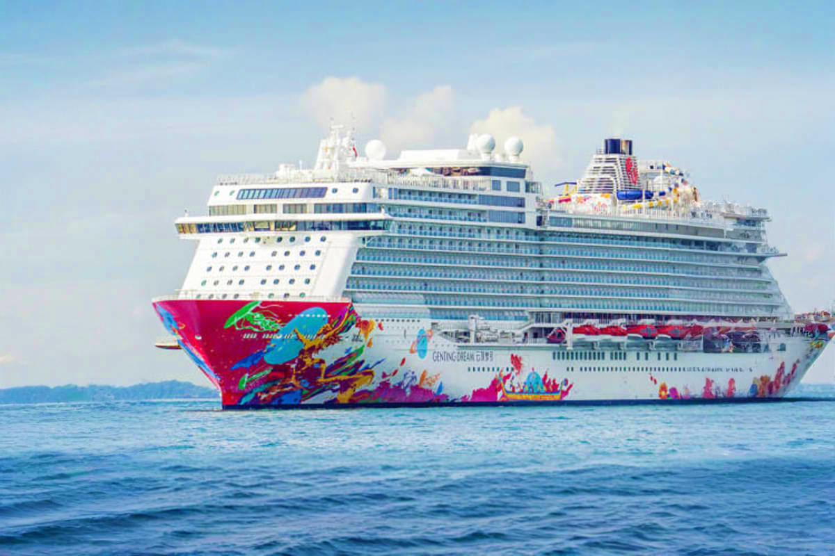 Genting Dream cruise ship with colorful red and blue hull artwork anchored in blue ocean waters under clear sky