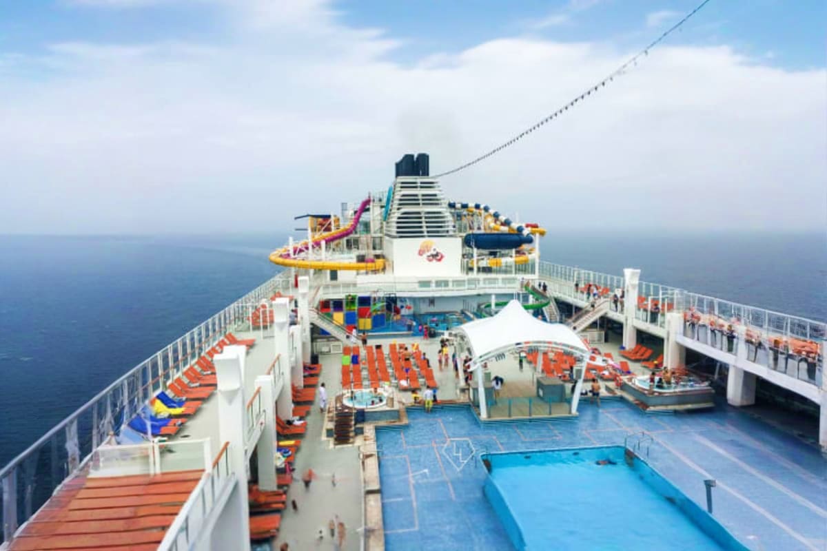 Aerial view of Genting Dream cruise ship deck with pools, lounging areas, water slides, and ocean horizon