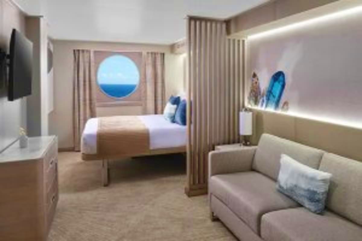 Norwegian Cruise Line Greek Islands Cruise Modern cruise ship stateroom with ocean view porthole, bed, sofa, and contemporary furnishings overlooking blue Mediterranean