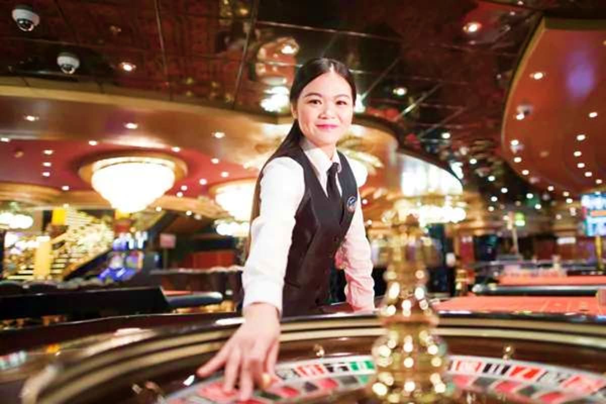 Female casino dealer standing at roulette table in upscale casino with red and gold decor and ambient lighting