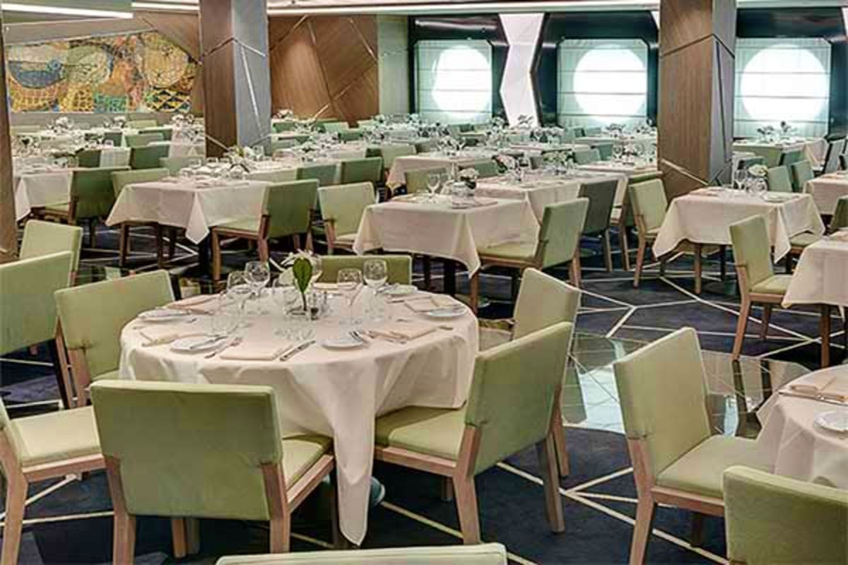 Elegant cruise ship dining room with round tables, cream tablecloths, green chairs, fine place settings, and large porthole w
