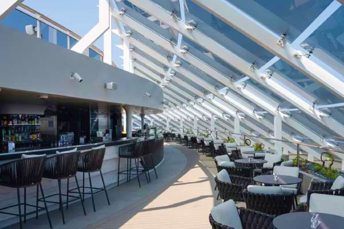 Modern rooftop bar and dining area on cruise ship with glass ceiling, lounge seating, and ocean views