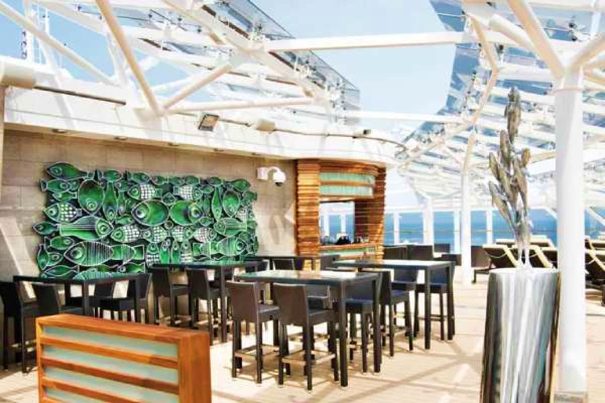 MSC Grandiosa Mediterranean Cruise Modern cruise ship outdoor dining area with high-top tables, green decorative wall art, glass roof panels, and ocean views