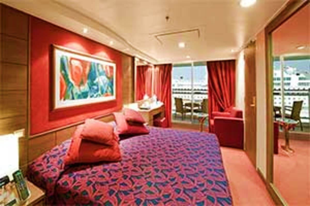 Luxurious cruise ship cabin with red accent walls, queen bed, modern furnishings, and ocean view balcony