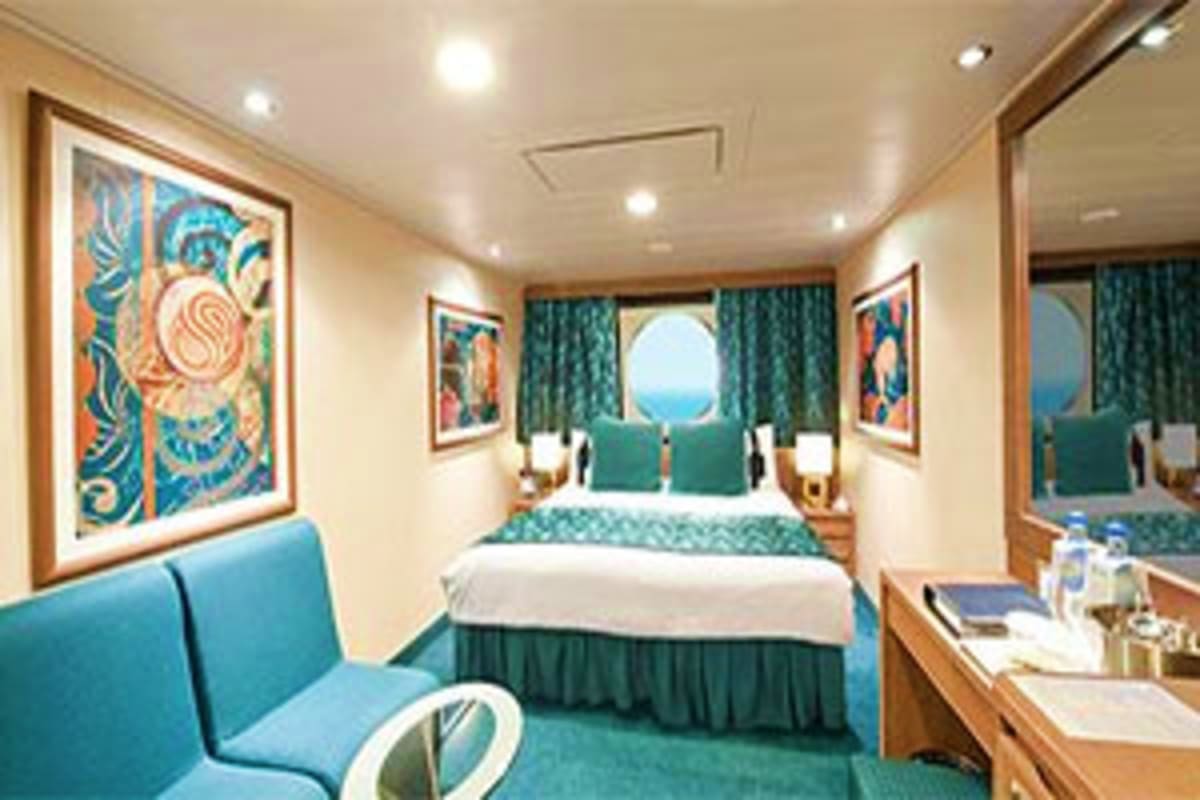 Luxury cruise ship cabin with queen bed, teal accents, porthole window with ocean view, and modern artwork