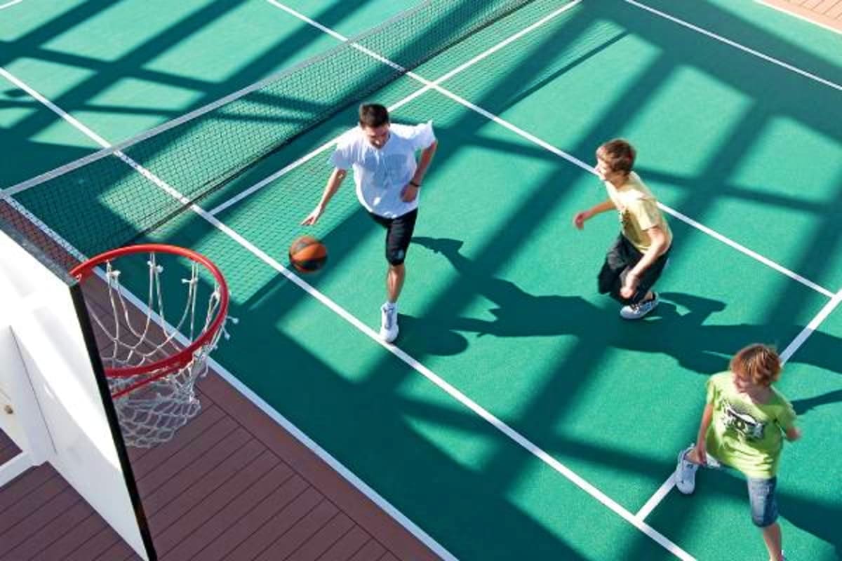 Overhead view of three children playing basketball on a teal outdoor court with red hoop and white court lines on a cruise sh