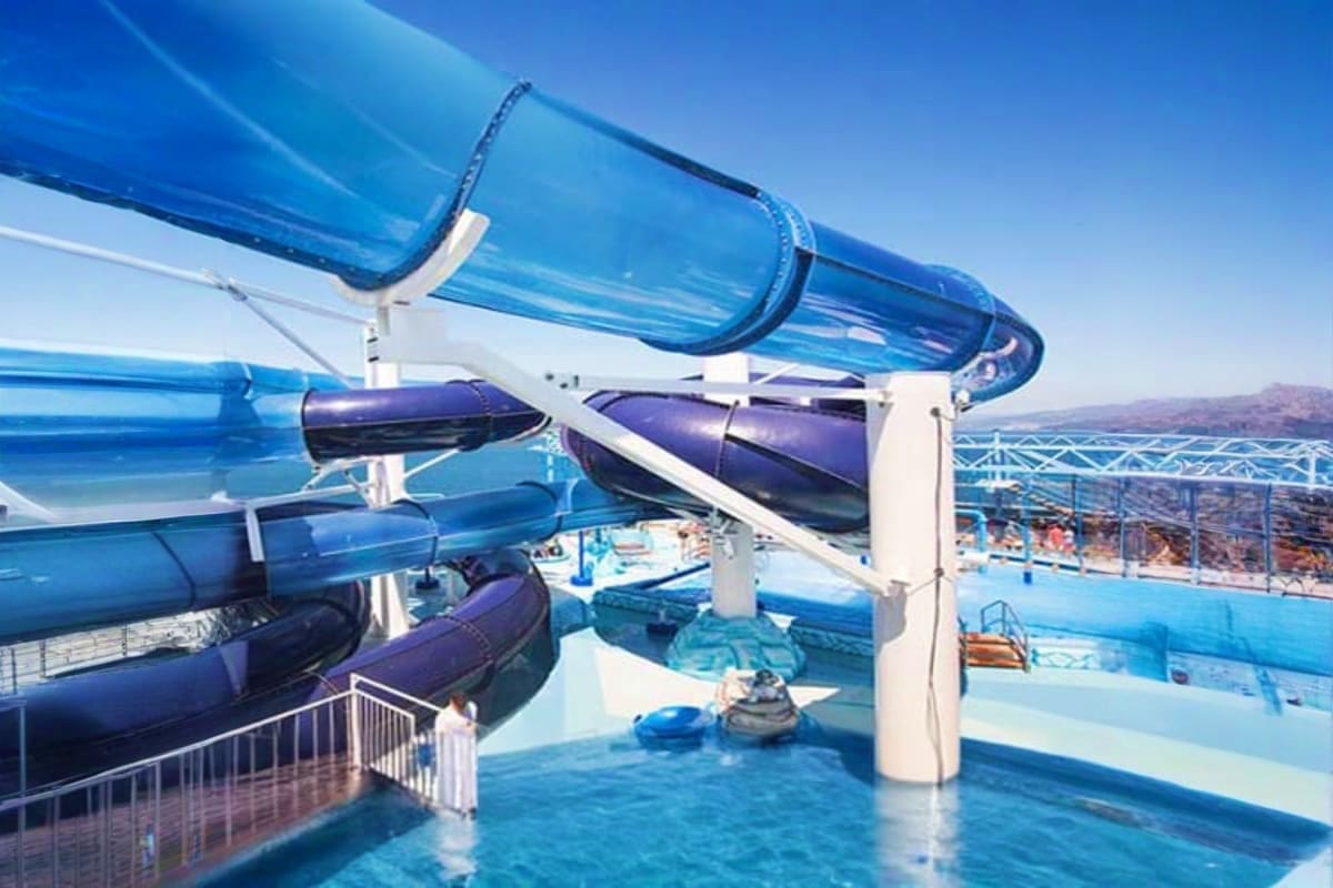 Blue water slides and pools at MSC Musica cruise ship recreational deck with mountain landscape in background