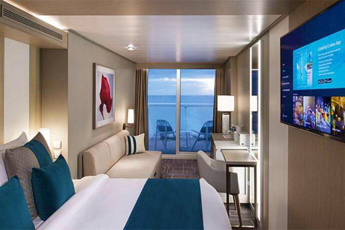 Modern cruise ship stateroom with bed, sofa, ocean view balcony, and flat-screen TV displaying streaming content