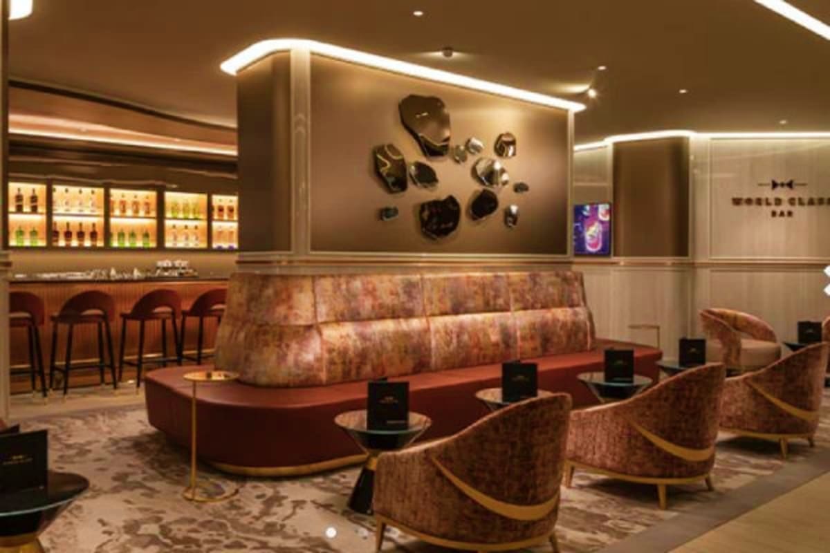 Modern upscale bar interior with curved red seating, decorative wall art, illuminated liquor shelves, and elegant lounge chai